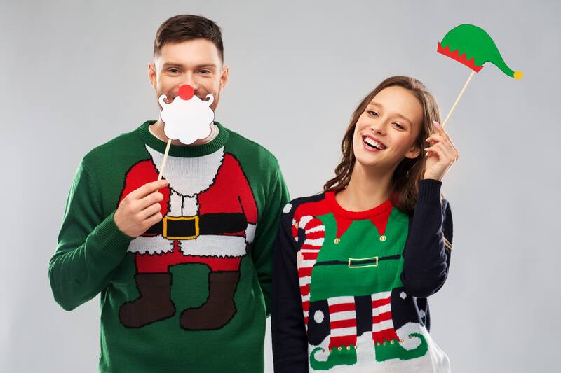 Couple in holiday sweaters posing with photo booth props